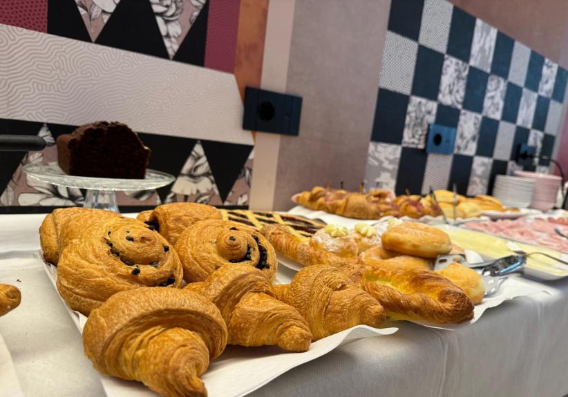 Buffet con croissant, dolci e affettati in una sala decorata.