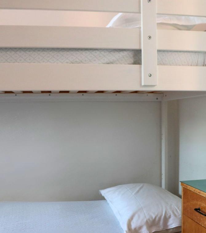 Letto a castello con biancheria bianca e comodino con pianta.