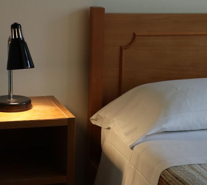 Lampada nera su comodino accanto a letto con lenzuola bianche.