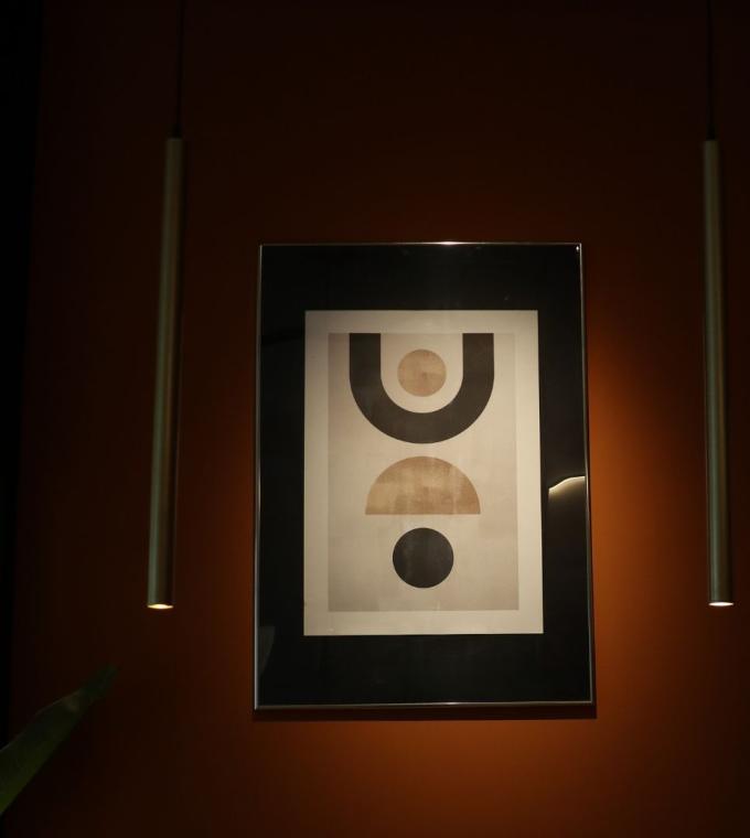 Quadro astratto con forme geometriche, illuminato da due lampade sospese.